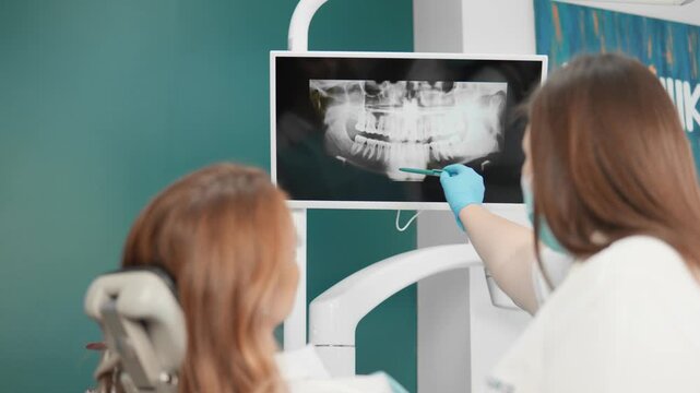 A dentist is examining a dental xray with a patient and explaining the treatment procedure in a dental clinic. It involves analysis, consultation, diagnosis, and a professional discussion