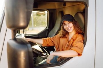 Young woman professional truck driver sitting and driving big truck cross country. Transport...