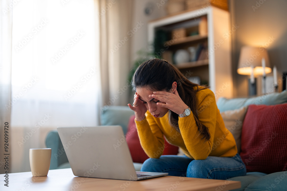 Wall mural a pensive caucasian woman in casual attire focuses on her laptop screen, displaying signs of worry a