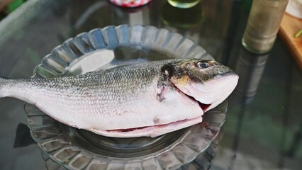 Fresh whole fish prepared for barbecue grilling on glass plate outdoors, ready for cooking seafood lovers, culinary experience