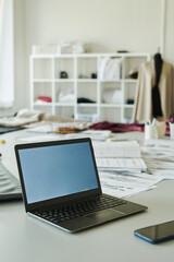Desktop computer and mobile phone on workplace of modern tailor or fashion designer with new attire and pattern sketches