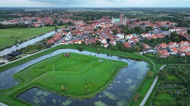 Aerial footage over Riberhus Castle Bank by historic town of Ribe, with the majestic Ribe Cathedral, red-tiled roofs, boats docked along the riverside, Denmark.
