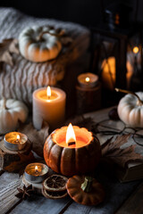Autumn composition with burning candles, mini munchkin pumpkins, warm wool knitted sweater on the wooden windowsill. Dark colours. Cozy home atmosphere, Thanksgiving decor, fall inspiration. Banner