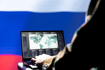 Russian army specialist working for Kremlin regime using target acquisition tech on laptop to detect enemy location. Ex KGB military officer isolated over Russia flag using satellite device