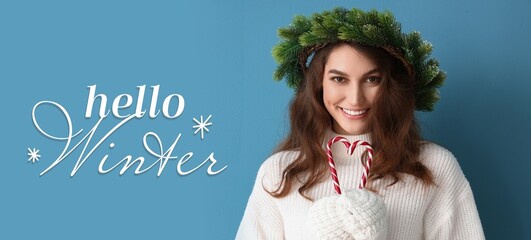 Stylish young woman in Christmas wreath and with candy canes on blue background. Hello, winter