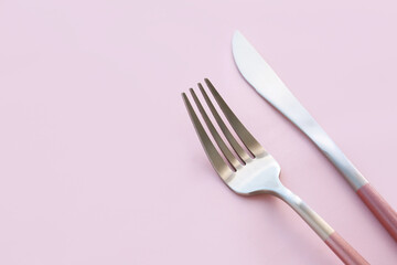 Stainless steel fork and knife on pink background