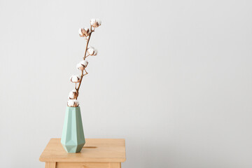 Cotton sprig in vase on stool near white  wall