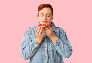 Young man eating piece of tasty pizza on pink background