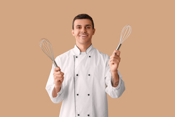 Naklejka premium Handsome happy male chef with whisks on brown background