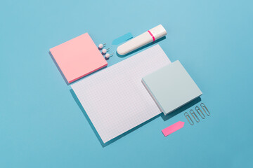 Highlighter, pen, push pins and paper sheets on blue background. Office and school supplies on blue...