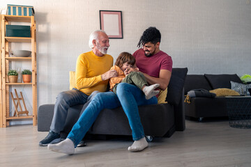 A cheerful senior man, his adult son, and a young boy revel in playful moments on a living room...