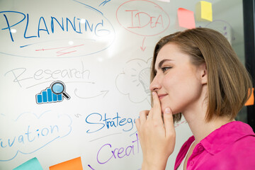 Young beautiful businesswoman putting sticker on glass board while finding a solution to solve financial problems by using mind map and colorful sticky note. Creative business concept. Immaculate.