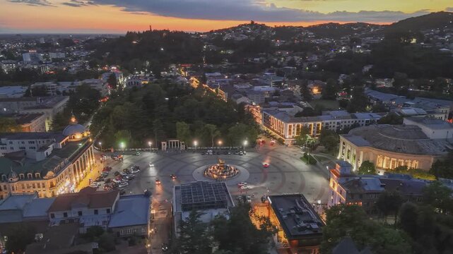 Aerial evening shot of Kutaisi with city lights, Georgia. Flying over Kutaisi old town with Colchis fountain on the main square. Sunset sky at background
