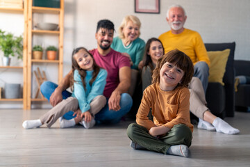 A diverse family smiles and poses in a cozy living room, with a young boy playfully sitting in...