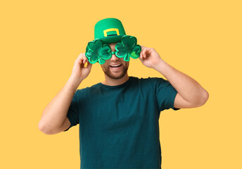 Happy young man in leprechaun's hat with party glasses on yellow background. St. Patrick's Day...