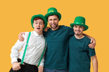 Happy young men in leprechaun's hats hugging on yellow background. St. Patrick's Day celebration