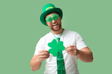 Happy young man in leprechaun's hat with party glasses and clover on green background. St....