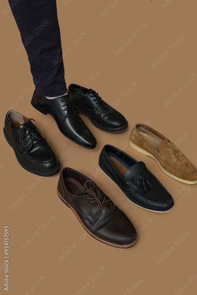 Wall mural Leg of young man with different stylish shoes on brown background