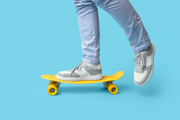 Legs of young man in stylish sneakers with skateboard on blue background