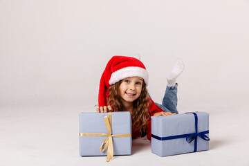 Cute little girl in Santa Claus hat lying with gift boxes. White background. Happy New Year and Christmas concept