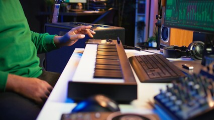 Music engineer producing song by mixing and mastering tunes on audio console, playing piano notes on synthesizer to record sounds on pc. Producer creating soundtracks with midi controller. Camera B.