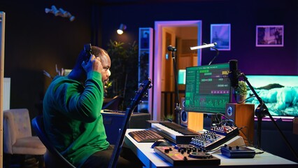 Producer creating a track by playing acoustic guitar in home studio, recording songs and singing on microphone. Sound engineer mixing and mastering his melody with stereo gear, soundtracks. Camera B.