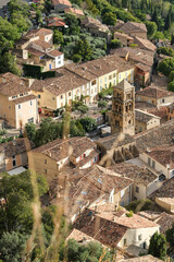An aerial view of a charming Mediterranean village with terracotta rooftops, narrow streets, and a historic church tower, surrounded by lush greenery. Moustiers-Sainte-Marie, France