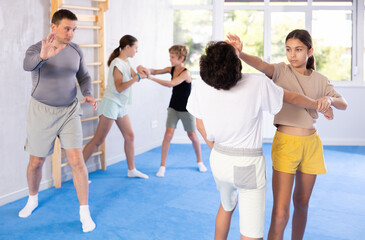 Boy and girl paired up and practice to aim stroke to neutralize opponent and repulse attack. Class self-defense training in presence of experienced instructor