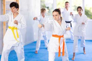 Group of boys and girls in kimonos train karate techniques in studio © JackF