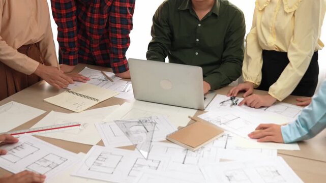 Architect and safety engineer discussion about building blueprint displaying on laptop on table with architectural document and wooden block scatter around at modern office. Closeup. Delineation.