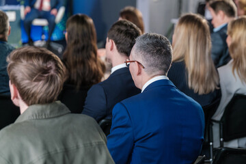 Business professionals seated in an audience listening to a speaker at a seminar or conference.