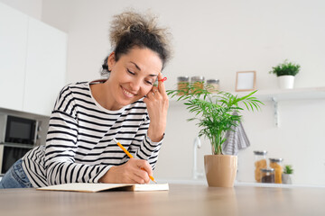 Beautiful middle-aged woman with red string on her finger writing something in notebook at home. Reminder concept