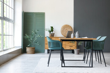 Interior of stylish room with dining table, folding screen and drawers