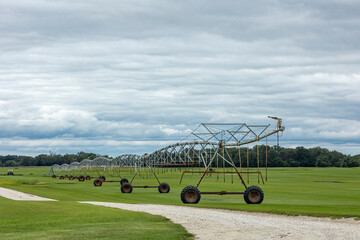 A center pivot irrigator along a field road in a field of grass sod on a cloudy day. 