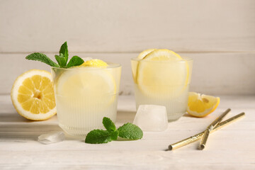 Glasses of fresh lemonade with mint and ice cubes on white wooden background
