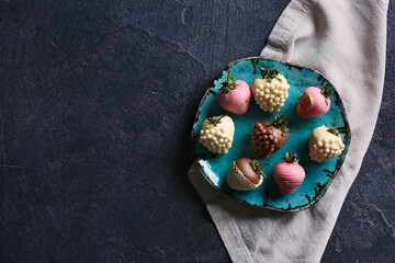Plate with chocolate covered strawberries on black background