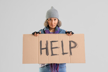 Mature homeless woman holding cardboard with word HELP on light background
