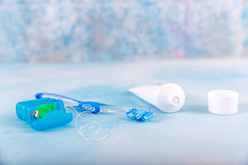 Dental floss and toothbrush on blue background. Tongue cleaner and other oral care products, dental...