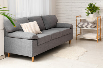 Cozy sofa with cushion and shelving unit in interior of living room
