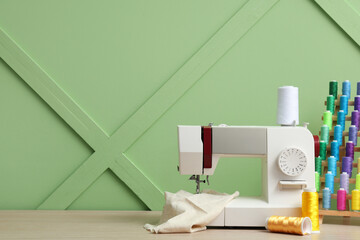 Modern sewing machine with set of colorful threads on green background