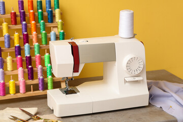 Modern sewing machine with set of colorful threads and tailor's supplies on yellow background