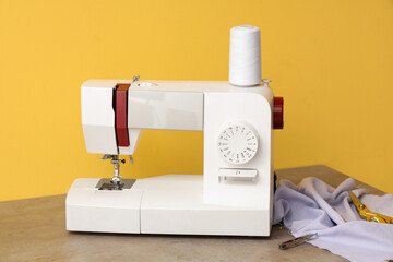 Modern sewing machine with fabric on yellow background