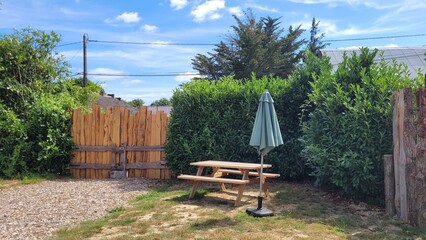 espace de pique nique avec table et parasol dans un milieu avec herbe et portail en bois