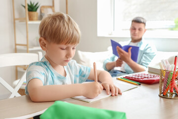 Cute boy taking dictation by his father in room