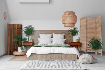Large bed, bedside tables and folding screen decorated with palm branches in bedroom