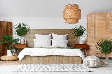 Large bed, bedside tables and folding screen decorated with palm branches in bedroom