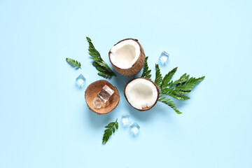 Halves of fresh coconut with ice cubes and leaves on blue background