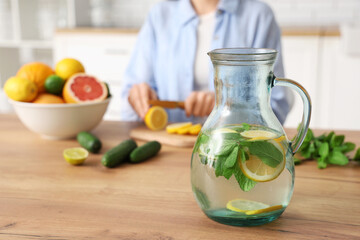 Young woman cutting lemon for preparing infused water in kitchen