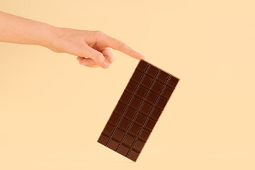 Female hand with sweet chocolate bar on yellow background