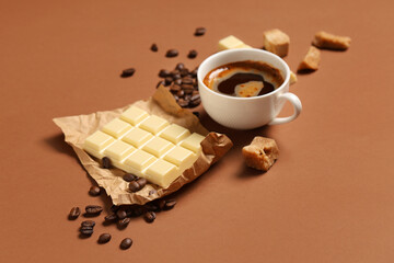 White sweet chocolate with cup of coffee and beans on brown background